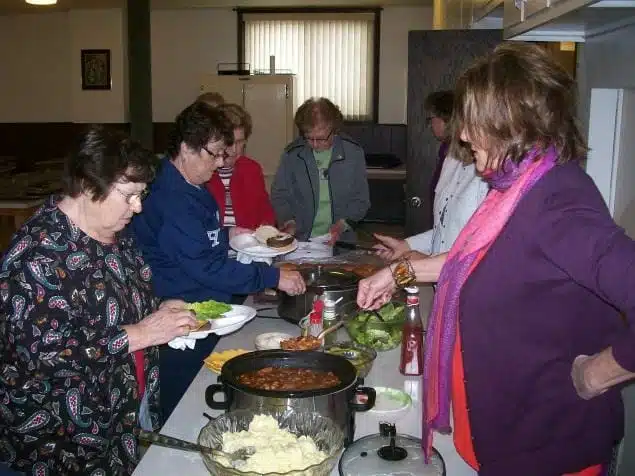 Seven individuals around a table making plates for a pot luck lunch.