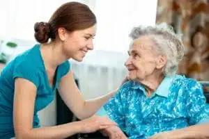 An elderly women looking at her caretaker who is smiling and touching her shoulder.